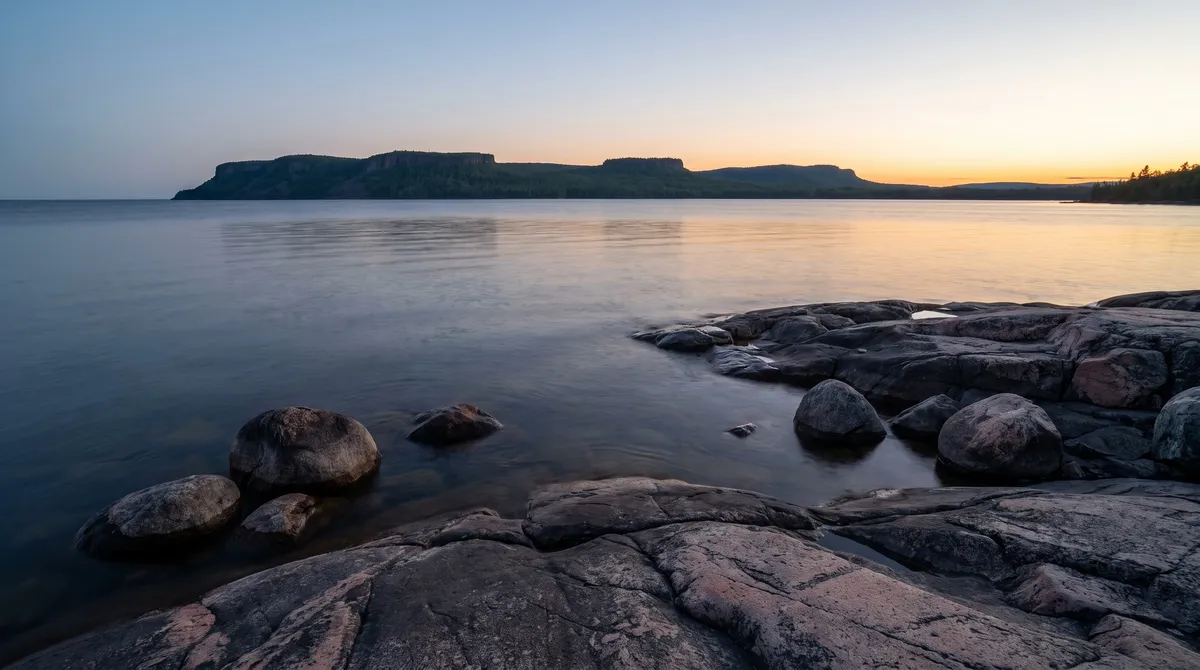 Illustration: dusk on a granite shore of Lake Superior, with a long flat-topped peninsula on the horizon across calm water.